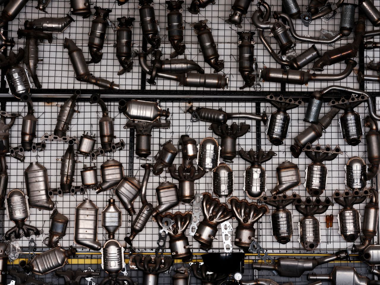 services-04 An array of automotive exhaust parts displayed on a grid wall in an industrial garage setting.