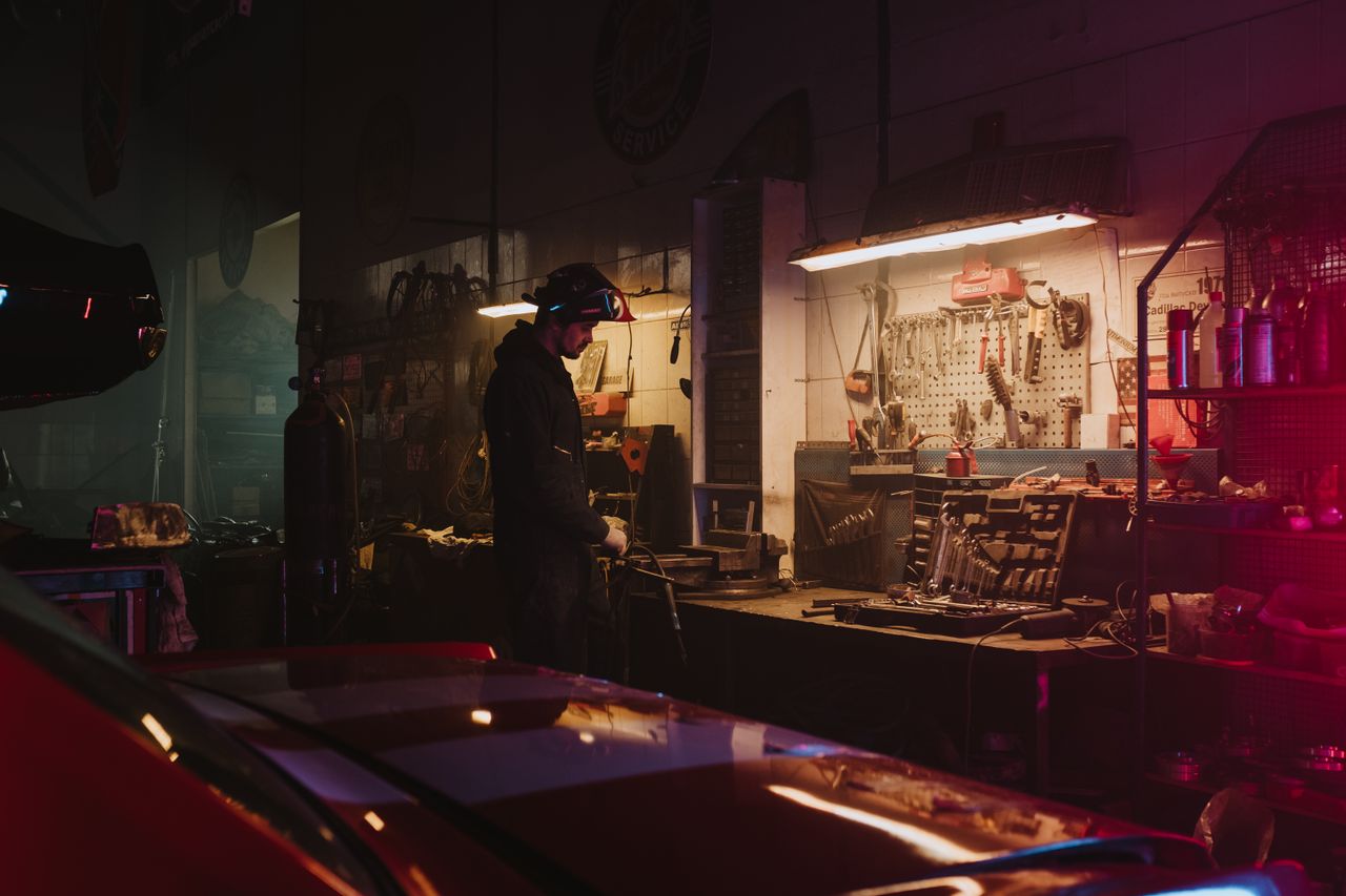 why-choose-us Mechanic working in a dimly lit garage workshop surrounded by tools and equipment.