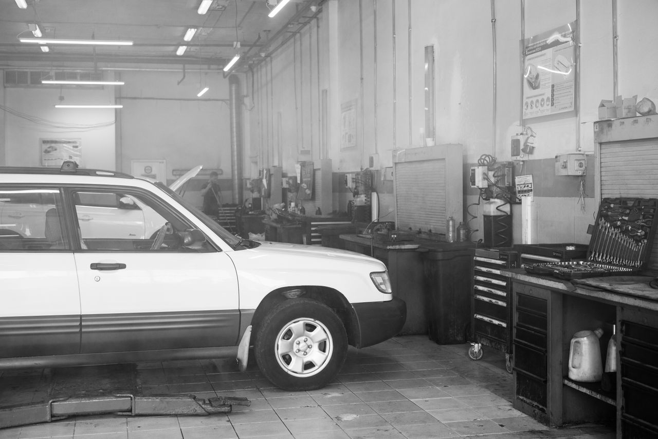 services-02 Black and white image of a car in a garage surrounded by tools and equipment.